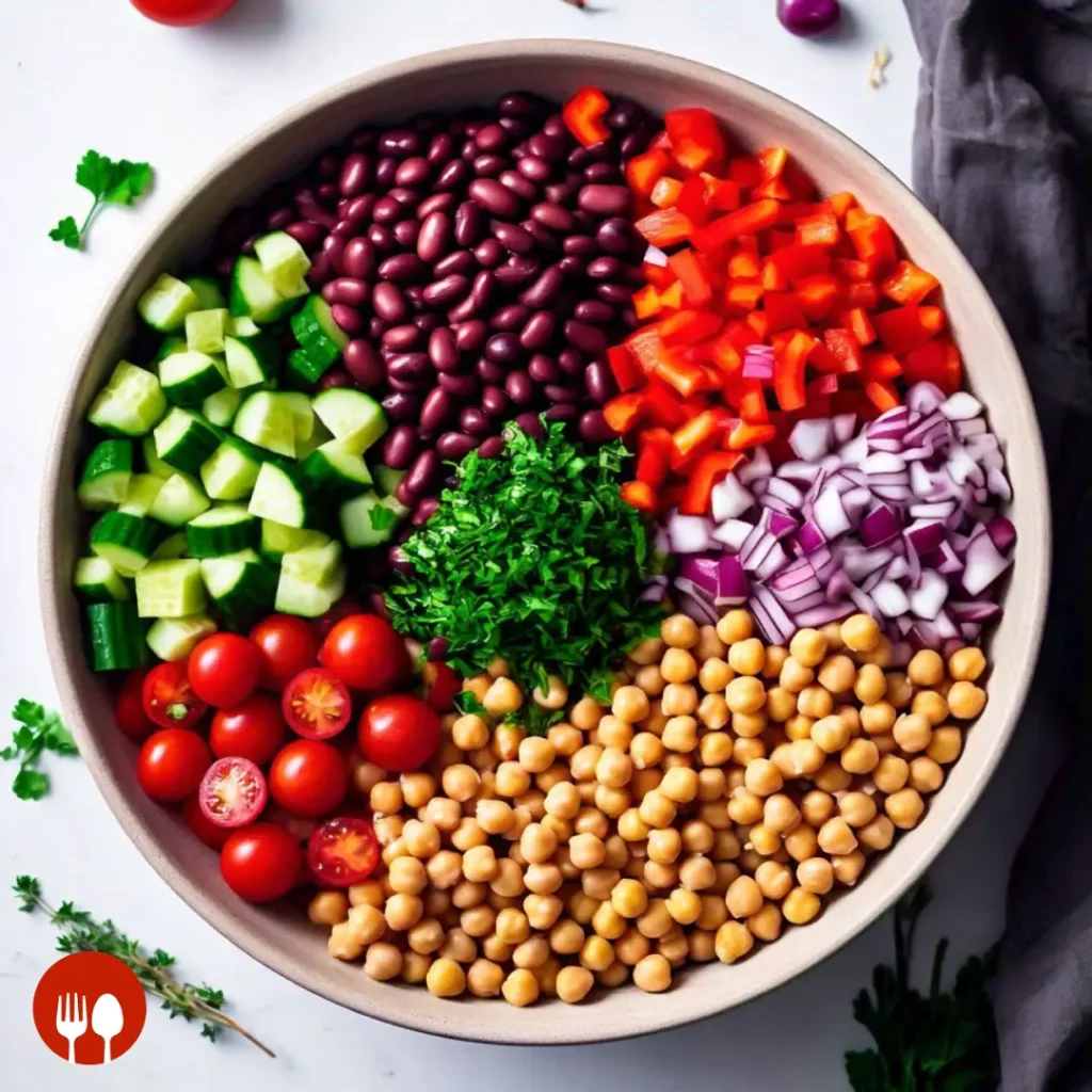 A mixing bowl filled with all the fresh ingredients for the dense bean salad, before tossing.